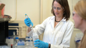 Person in lab coat and safety goggles in a lab. 