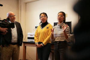 Three people wearing lab safety glasses stand and have a conversation. 