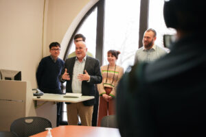 Group of people standing behind another person in forefront who is speaking. 