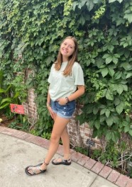 Smiling person standing in front of an ivy-covered wall.