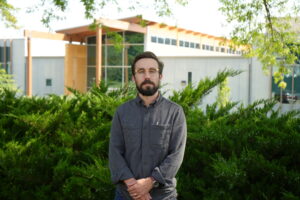 A headshot of Joel Stokdyk standing outside in front of green bushes