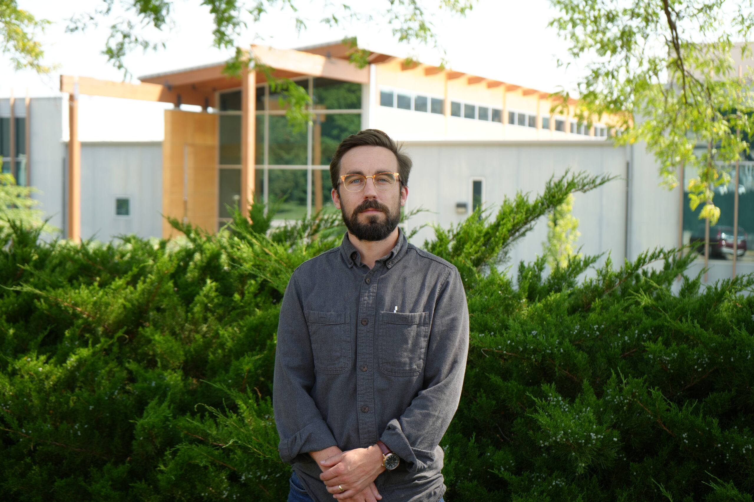 A headshot of Joel Stokdyk standing outside a building in front of green bushes