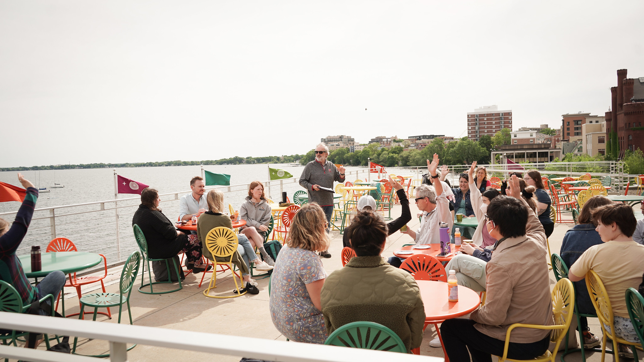 large group of people sitting at tables outdoors with a lake in the background